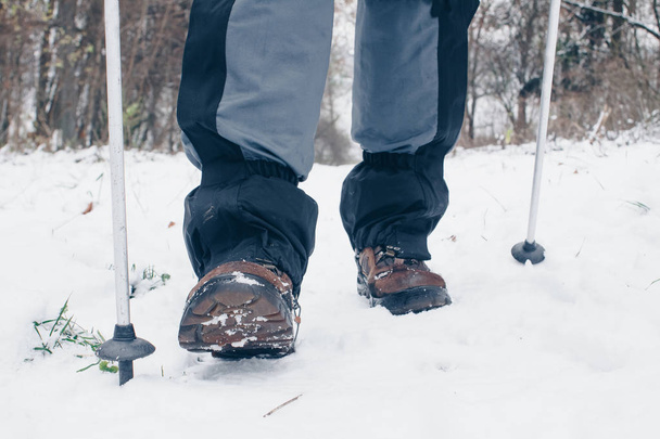 De wandelaar laarzen met trekking palen en beenkappen gaan vooruit in het winter forest - Foto, afbeelding