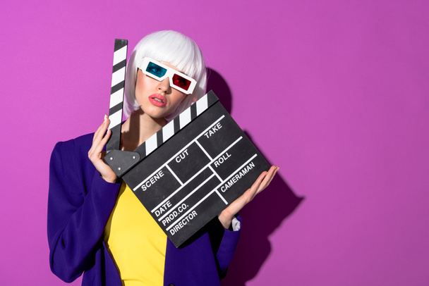Girl in white wig and 3d glasses holding clapperboard on purple background - Valokuva, kuva