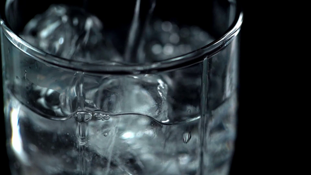 близкий обзор прозрачной воды, наливающейся в прозрачное стекло с кубиками льда, изолированными на черном
 - Кадры, видео