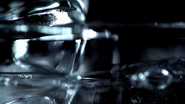 selective focus of clear water pouring into transparent glass with ice cubes isolated on black - Metraje, vídeo