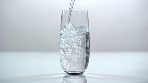 Studio πυροβολούν νερό ρίχνει σε διαφανές γυαλί, σε λευκό φόντο - Πλάνα, βίντεο