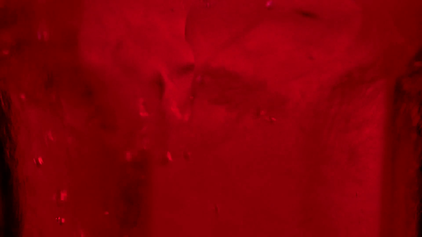 Close-up van rode vloeistof gieten in glas met ijsblokjes en water - Video