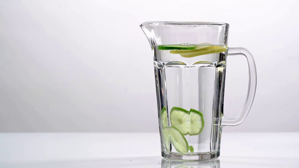 sesión de estudio de agua clara en jarra de vidrio con lima verde y rodajas de limón amarillo sobre fondo blanco
 - Metraje, vídeo
