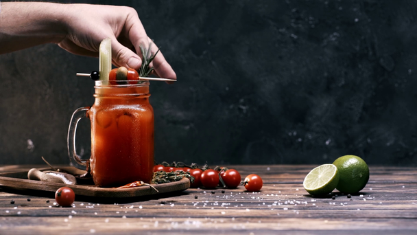 cropped view of man putting rosemary in red cocktail on wooden table  - Materiał filmowy, wideo
