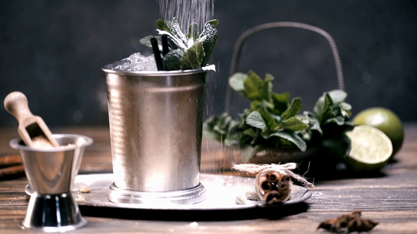 selective focus of sugar powder scattering on mojito cocktail with ice cubes, mint and lime in silver glass on wooden table - Footage, Video