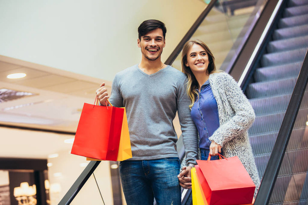 Happy νεαρό ζευγάρι ψώνια και κρατώντας τσάντες σε εμπορικό κέντρο - Φωτογραφία, εικόνα