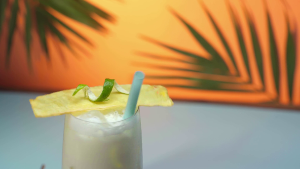 Крупный план коктейля пина-колада в мокром стекле с декорацией, вращающейся на оранжевом фоне с зелеными пальмовыми листьями
 - Кадры, видео