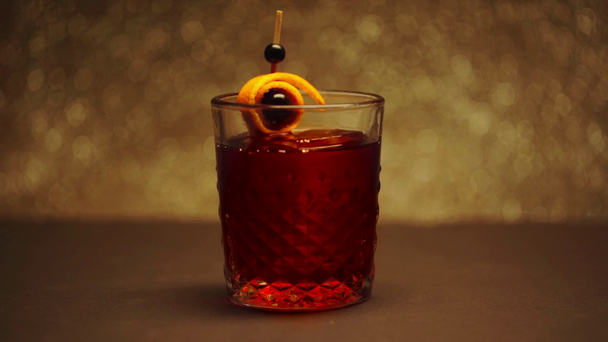 pincho con bayas y cáscara de naranja cayendo en vidrio con gran cubo de hielo y cóctel rojo
 - Metraje, vídeo