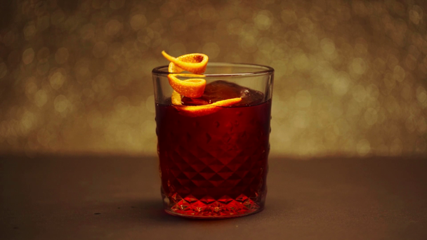 cáscara de naranja cayendo en vidrio con gran cubo de hielo y cóctel rojo
 - Imágenes, Vídeo