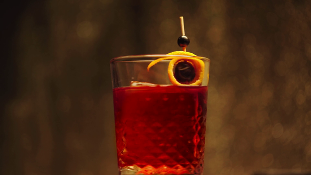 cóctel rojo en vaso con bayas y cáscara de naranja en pincho giratorio sobre fondo oscuro
 - Imágenes, Vídeo