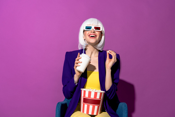 Laughing girl in 3d glasses eating popcorn and drinking soda on purple background - Foto, Imagen