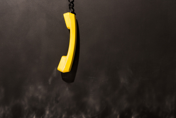 Auricular amarillo con alambre negro colgando sobre fondo oscuro
 - Foto, Imagen