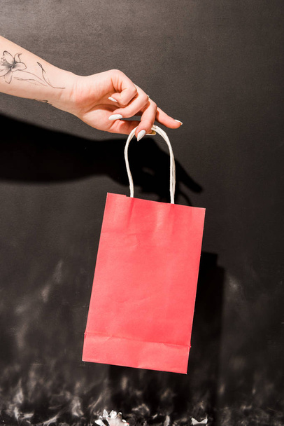 Cropped view of girl with tattoo holding red shopping bag on black background - 写真・画像