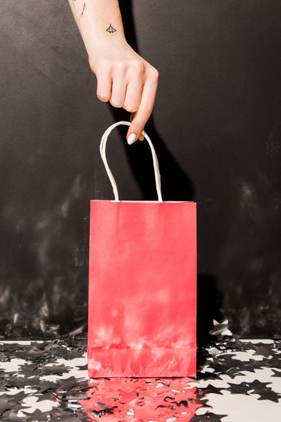 Partial view of girl with tattooes holding pink shopping bag on black background - Foto, Imagem