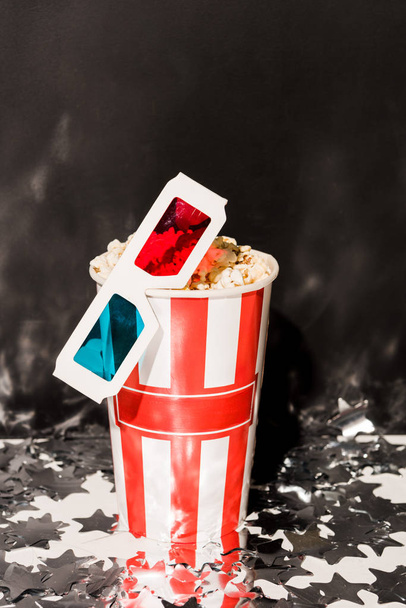 Cup with popcorn and 3d glasses on dark background - Photo, Image