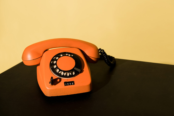 Teléfono naranja viejo parado en la superficie negra sobre fondo amarillo
 - Foto, Imagen