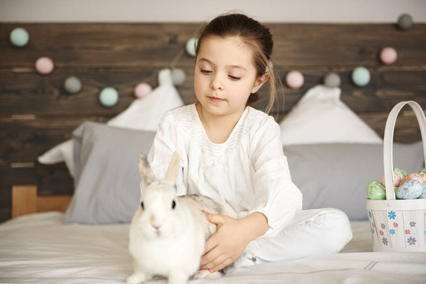 Girl and rabbit sitting on bed  - Foto, Imagen