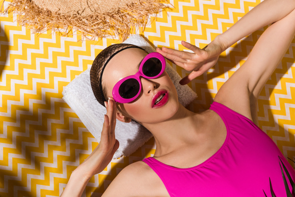 Woman in sunglasses and swimsuit lying on towel on yellow background - Foto, Imagen