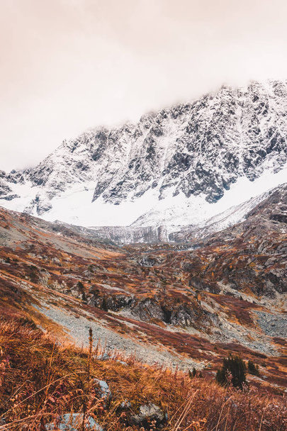 Redhaired hegyoldal. Sárga fű őszi-völgyben. Sziklák alatt a hó a láthatáron. - Fotó, kép