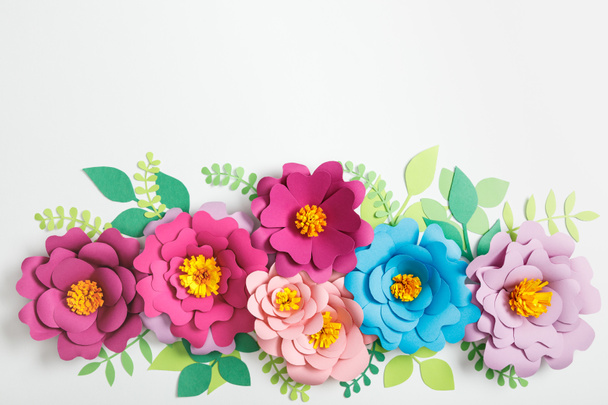 top view of multicolored paper flowers and green leaves on grey background - Foto, Imagen