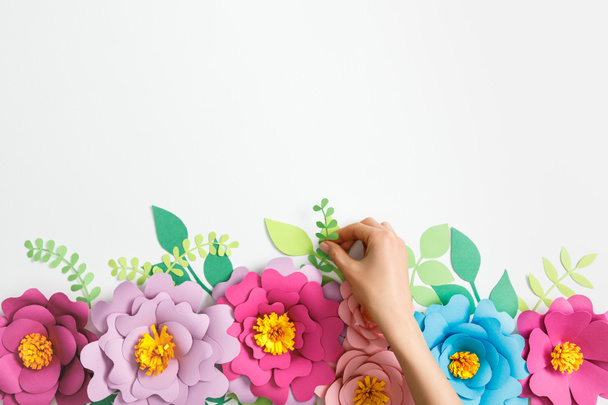 cropped view of woman putting green plant near multicolored paper flowers on grey background - Foto, Imagem