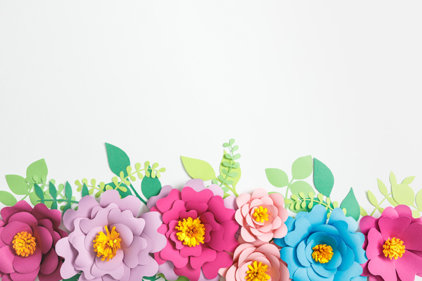 felülnézet színes papír virágok és zöld levelek a szürke háttér - Fotó, kép