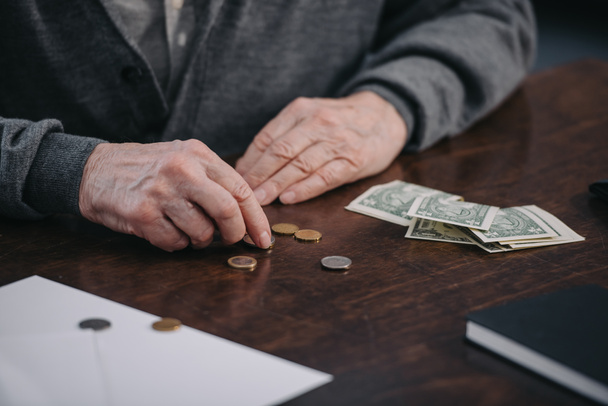 cropped view of senior man sitting at table and counting money - Foto, Imagen