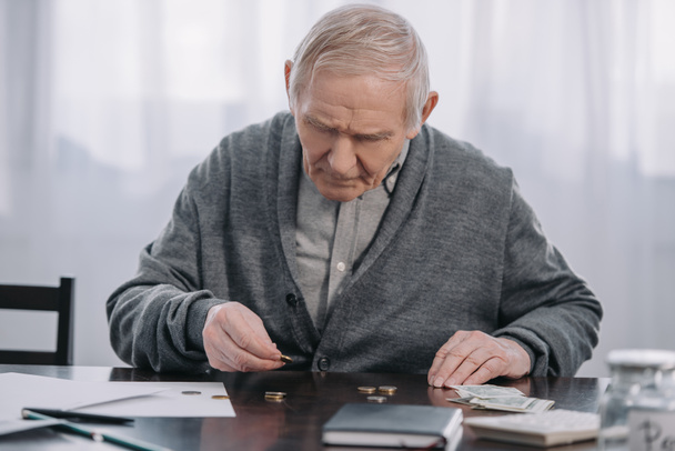 senior man sitting at table and counting money at home - Foto, Imagen