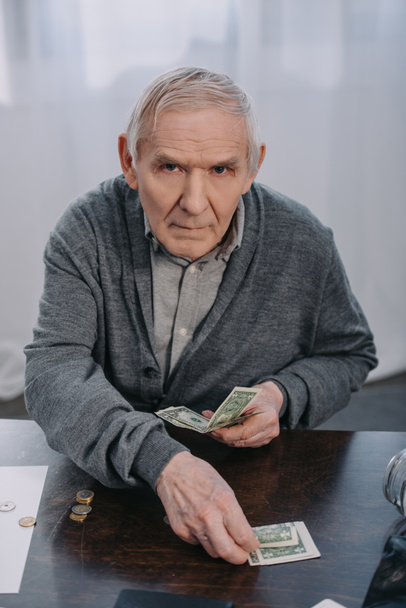 Senior sitzt am Tisch, schaut in die Kamera und zählt zu Hause Geld - Foto, Bild