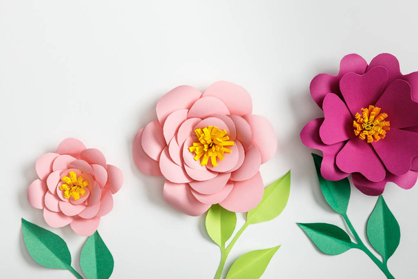 top view of pink paper flowers and green plants with leaves on grey background - Foto, immagini