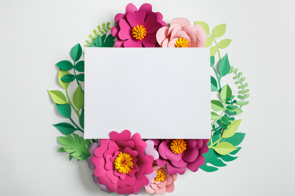 top view of white blank card near paper flowers with green leaves on grey background - Fotografie, Obrázek