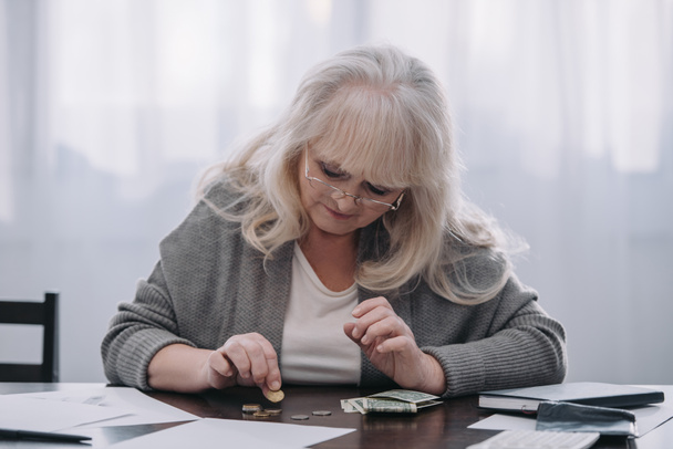 female pensioner sitting at table and counting money at home - Фото, изображение