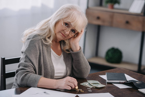 smutná žena důchodce sedí u stolu, při pohledu na fotoaparát a počítání peněz doma - Fotografie, Obrázek