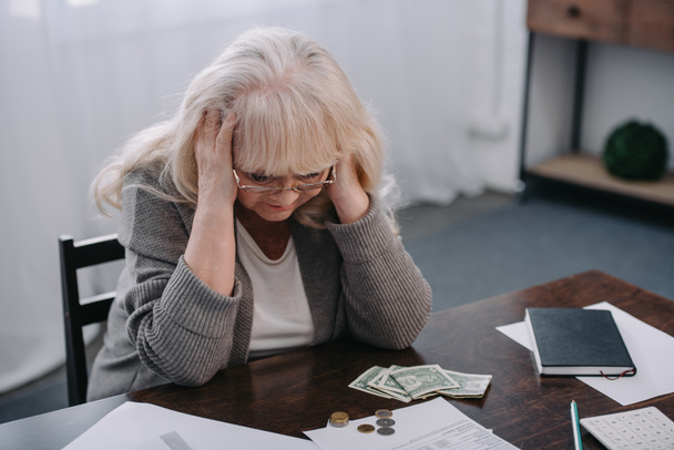 stanca donna anziana con le mani sulla testa che ha mal di testa mentre conta i soldi a casa
 - Foto, immagini