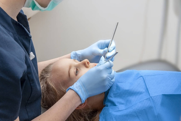 El dentista corrige el diente para una niña en un fondo claro
 - Foto, Imagen