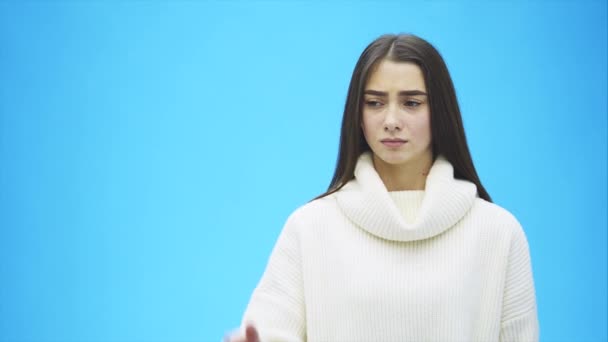 It is interesting that a young woman in a knitted white sweater. From amazement he raises his hand up and puts it on his head. Isolated against a background of a blue wall, a portrait of a studio. The - Video, Çekim