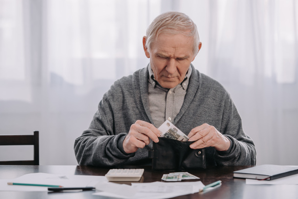 pensionista masculino sentado en la mesa con papeleo y poner dinero en la cartera
  - Foto, Imagen