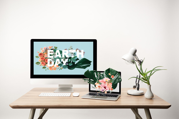 Föld nap illusztráció a idegen rádióadást figyel számítógép és laptop-val monstera levelek és virágok ábrán látható a képernyőn, a fából készült asztal - Fotó, kép