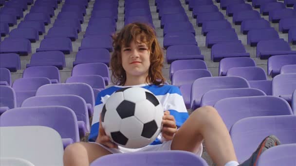 Jonge jongen voetballer met voetbal op de tribunes van het stadion, 4k - Video