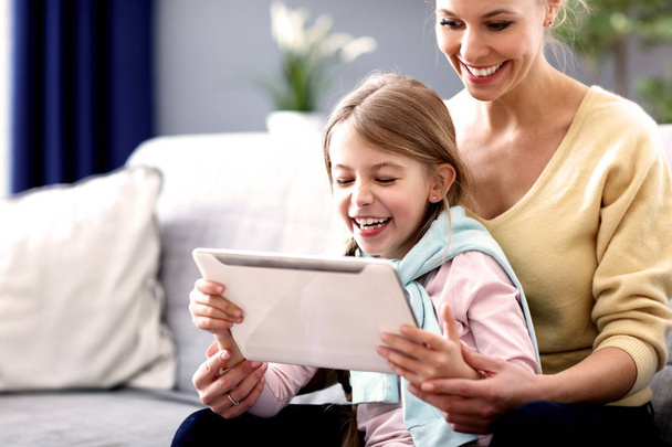 Little girl and her mom using tablet while sitting on sofa at home - Φωτογραφία, εικόνα