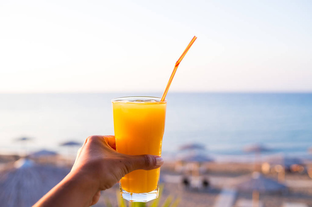 Orange juice with pulp in hands on the beach, detox time,healthy eating,Diet concept.Hand with fresh tasty freshly-squeezed juice of ripe oranges in glass. Calm sea and the horizon.juice glass with st - Fotoğraf, Görsel