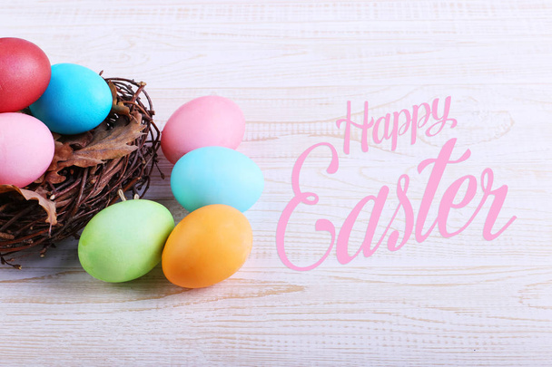 Colored Easter eggs in a nest, on a white wooden table. Text, happy easter. - Foto, immagini