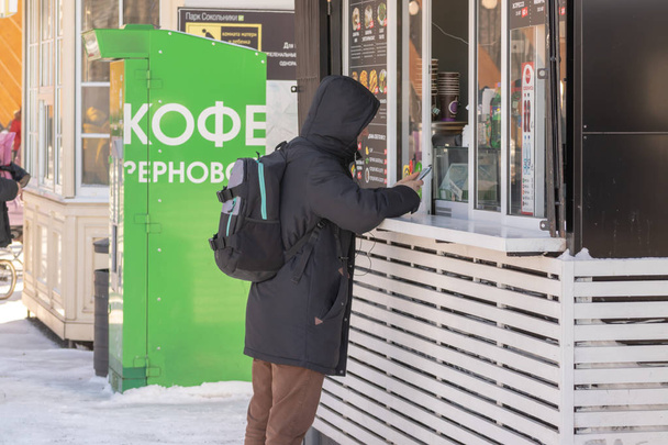 Moskou, Rusland - 02 maart 2019: Een man straat fast food en warme dranken in de stal te kopen tijdens een wandeling in een stadspark in de winter, fastfood te eten voor onderweg - Foto, afbeelding