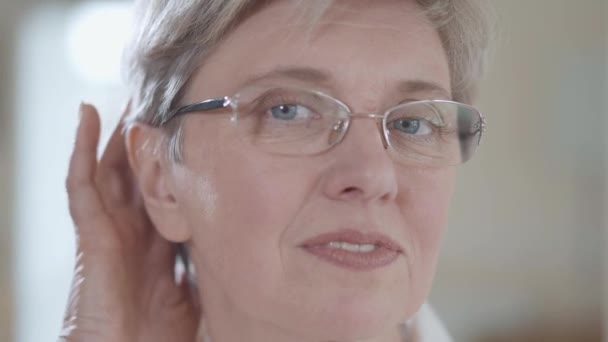 Portrait of attractive senior woman with glasses looking in camera fixing her hair with pleasent smile indoors close up. Lady takes off glasses. - Záběry, video