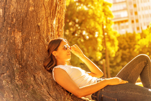 A young woman lying next to a tree and enjoying the sunshine - Zdjęcie, obraz