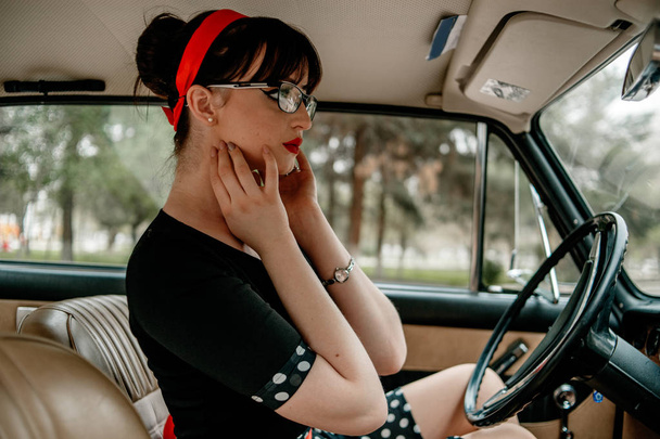 Portrait of a young beautiful girl in retro dress in vintage car - Photo, Image