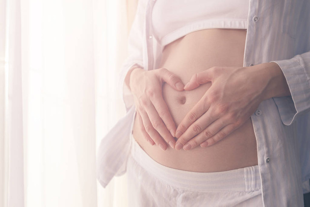 έγκυος κορίτσι με τα χέρια σε σχήμα καρδιάς στην κοιλιά - Φωτογραφία, εικόνα