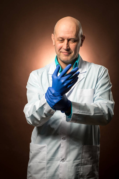 Medico esperto anni '50 indossa un cappotto bianco, indossa guanti di gomma blu e sorride
 - Foto, immagini