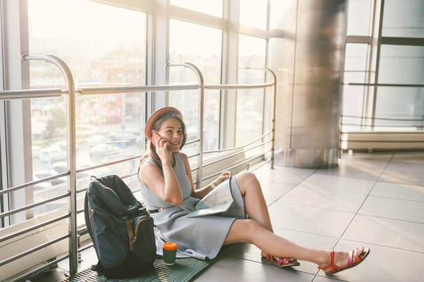 teema matkailu ja nuorten opiskelijoiden matkustaminen. Kaunis nuori valkoihoinen tyttö mekko ja hattu istuu lattialla turisti matto sisällä terminaalin lentokentän terminaali. Odotushuone viivästynyt lento, lähtö viivästynyt
 - Valokuva, kuva
