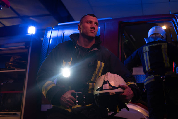 Die Feuerwehr kam in der Nacht zu dem Einsatz. schöner Feuerwehrmann, der eine Schutzuniform mit Taschenlampe trägt - Foto, Bild